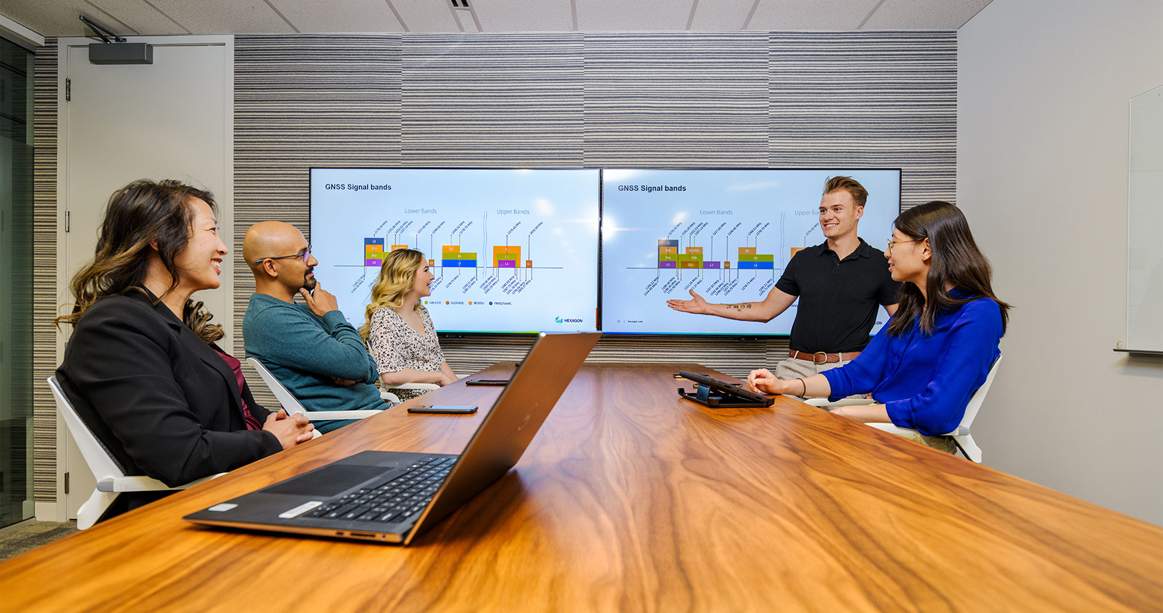 Employees sitting at a conference table looking at a diagram of GNSS bands and frequencies